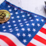 Moeda dourada de Bitcoin sobre bandeira dos Estados Unidos ao lado de uma caneta esferográfica