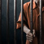 homem de uniforme laranja atrás das grades na prisão