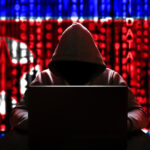 Pessoa com rosto coberto por capuz mexendo em um notebook -ao fundo a bandeira da Coreia do Norte com traços cibernéticos