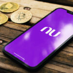 Sob um banco de madeira três criptomoedas ao lado de um celular com logo do Nubank