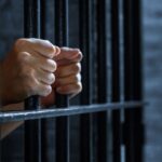 mãos seguram por dentro grade de cela de prisão